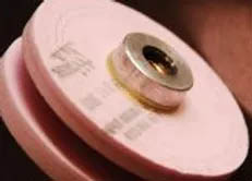 Pink circular grinding wheel or polishing disc with metal center attachment for power tools.